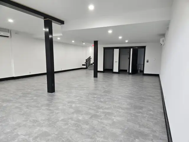 Finished basement with grey vinyl plank floor, black trim, recessed lights and a wrapped support post