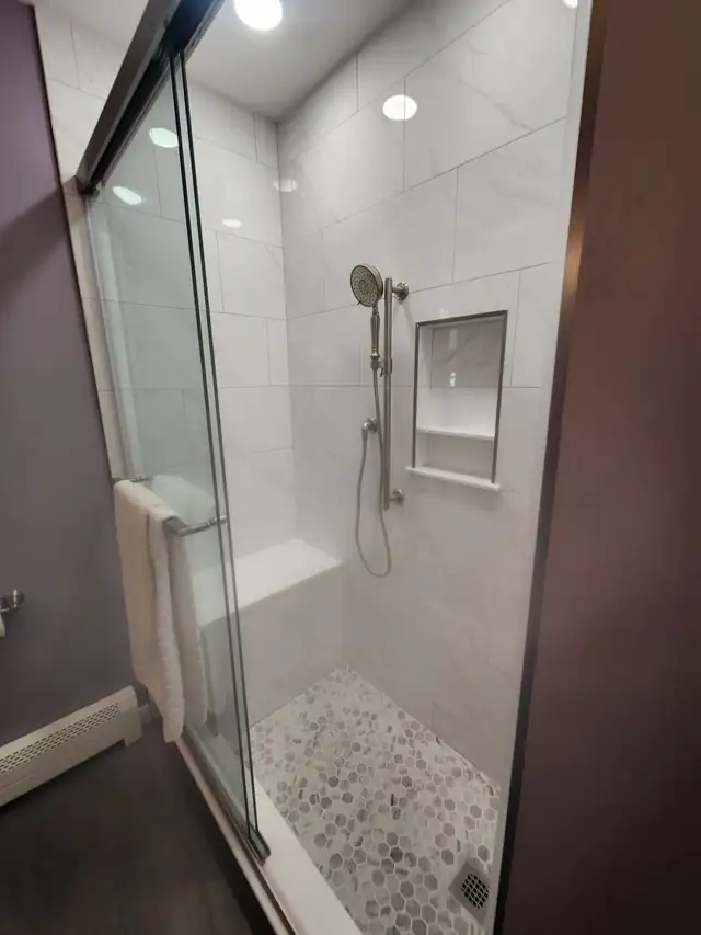 Large-format white tile shower with a recessed niche, handheld shower and pebble tile floor