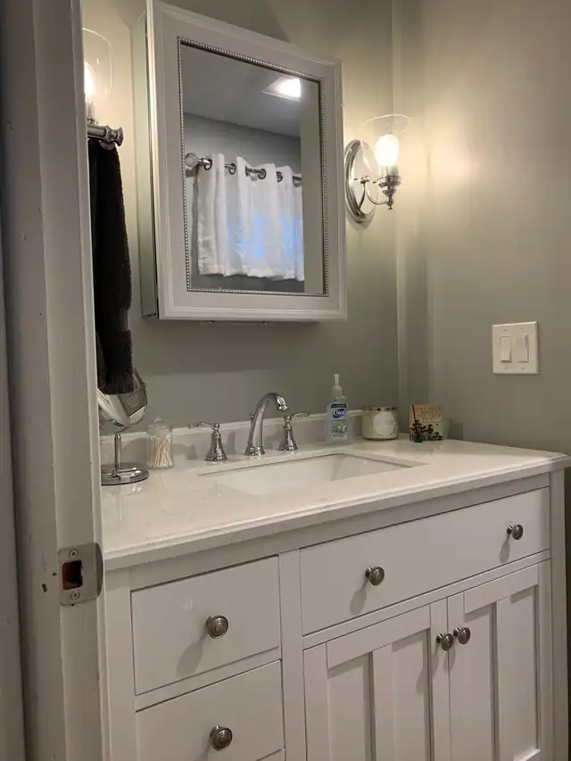 Remodeled master bathroom with a white vanity, white stone-look top, chrome faucet and framed mirror