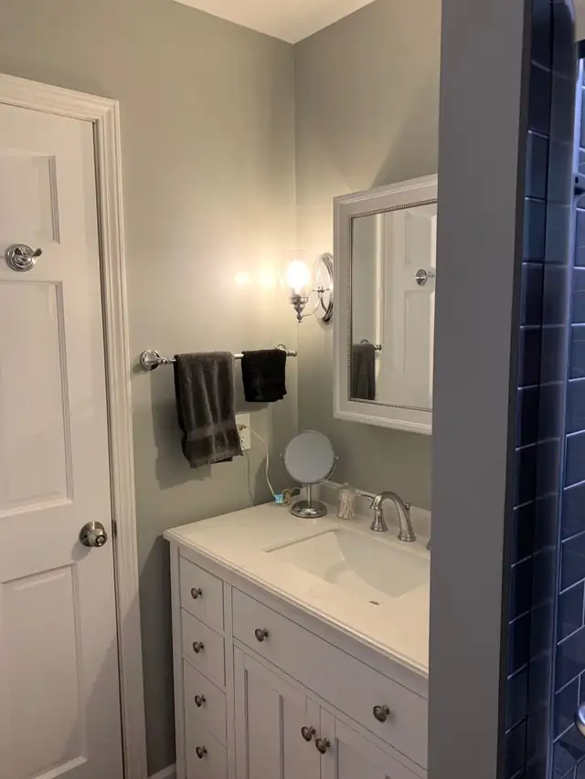 White vanity with drawers, grey walls and a dark subway tile shower wall